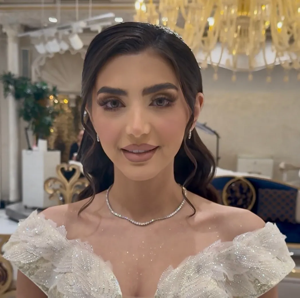 Bride with soft glam makeup, fluttery lashes, a mauve-nude lip and a crystal headpiece, smiling at the camera